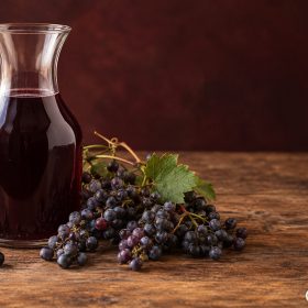 Bình thủy tinh rượu nho tím cạnh chùm quả tươi đã xác định nguồn gốc