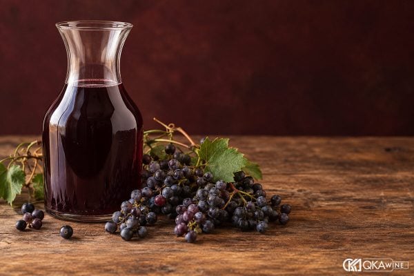 Bình thủy tinh rượu nho tím cạnh chùm quả tươi đã xác định nguồn gốc