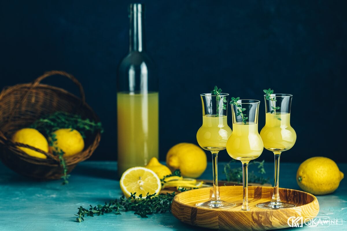 Ba ly limoncello nhỏ trên khay gỗ cạnh chai rượu và chanh vàng