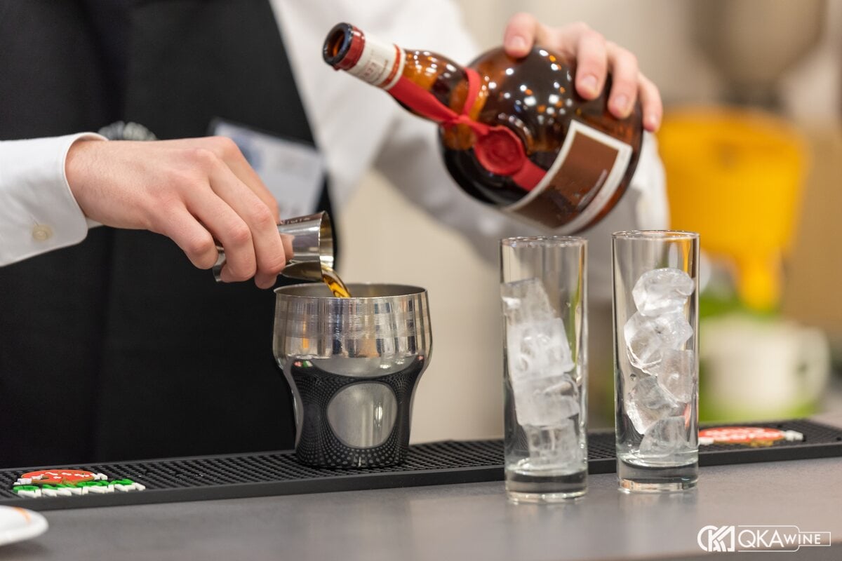 Bartender đong rượu mùi cam từ chai vào jigger tại quầy bar