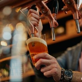 Bartender kéo cần rót bia tươi từ vòi vào ly tại quầy bar