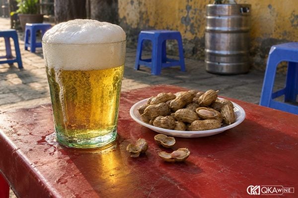 Cốc bia cỏ thủy tinh xanh đầy bọt cạnh đĩa lạc luộc