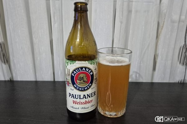 Chai bia Paulaner Weissbier cạnh ly bia vàng đục trên bàn gỗ