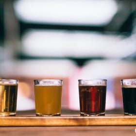 Bốn ly bia từ vàng nhạt tới đen xếp hàng trên khay gỗ ở quầy bar