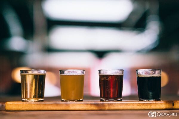 Bốn ly bia từ vàng nhạt tới đen xếp hàng trên khay gỗ ở quầy bar