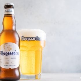 Chai bia Hoegaarden đặt cạnh ly lục giác đầy bia trắng đục