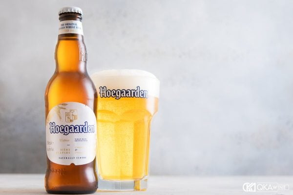 Chai bia Hoegaarden đặt cạnh ly lục giác đầy bia trắng đục