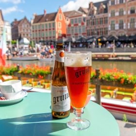 Chai và ly bia Bỉ màu hổ phách trên bàn quán bên bờ kênh ở Ghent