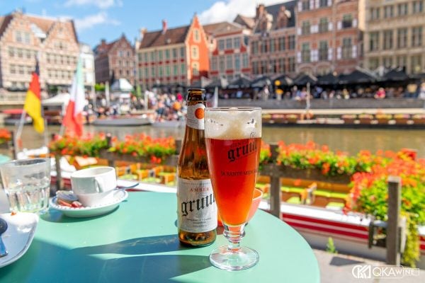 Chai và ly bia Bỉ màu hổ phách trên bàn quán bên bờ kênh ở Ghent