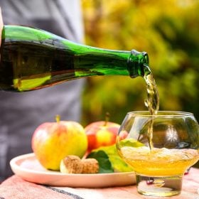 Rót cider từ chai vào ly cạnh đĩa táo ngoài vườn