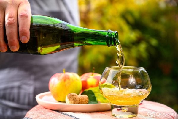 Rót cider từ chai vào ly cạnh đĩa táo ngoài vườn