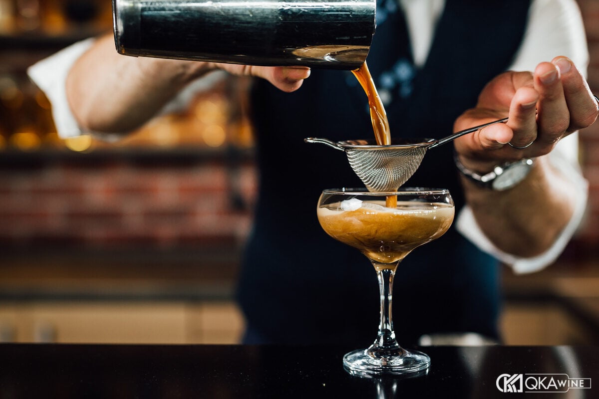 Bartender lọc cocktail qua rây vào ly coupe tại quầy bar