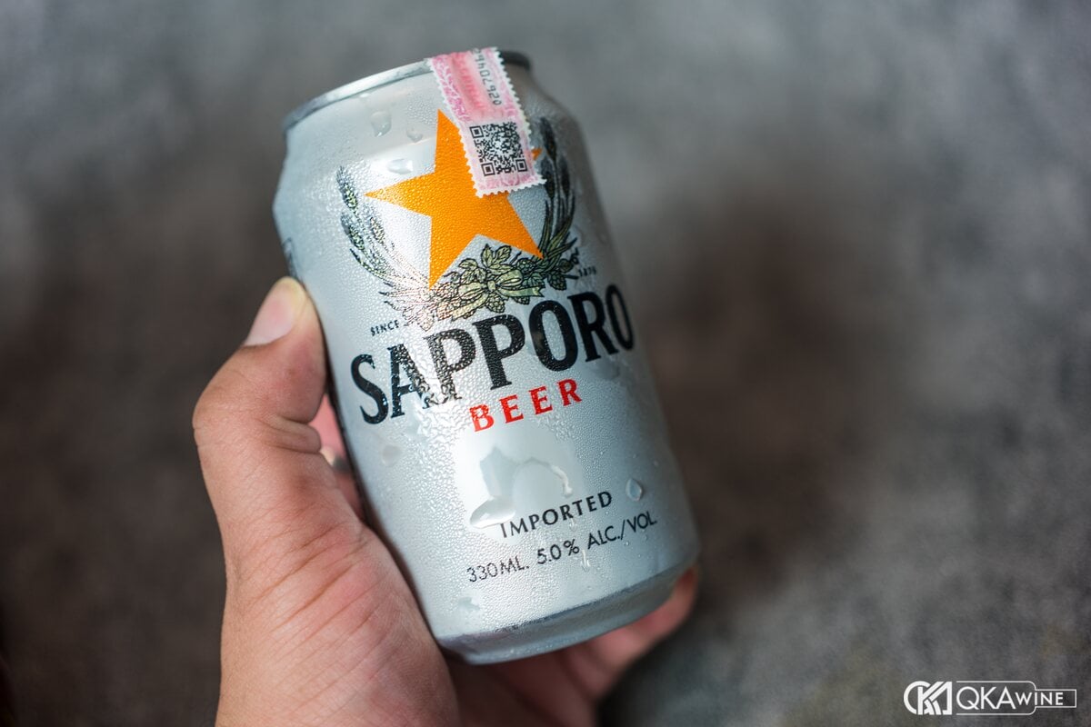 Bàn tay cầm lon bia Sapporo màu bạc có ngôi sao vàng
