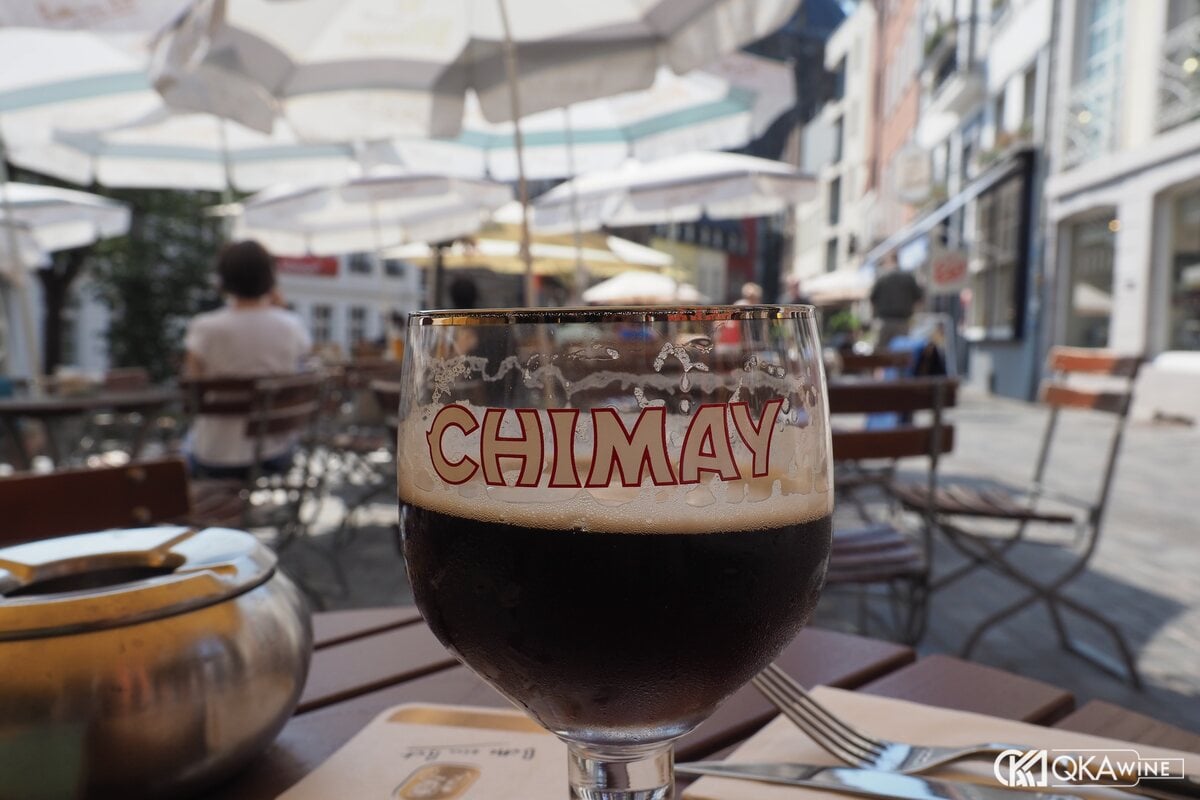 Ly chalice in chữ Chimay chứa bia nâu sẫm trên bàn quán ngoài trời