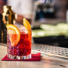 Ly Negroni đỏ cam với lát cam trên quầy bar