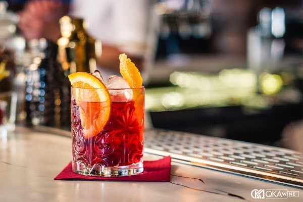 Ly Negroni đỏ cam với lát cam trên quầy bar