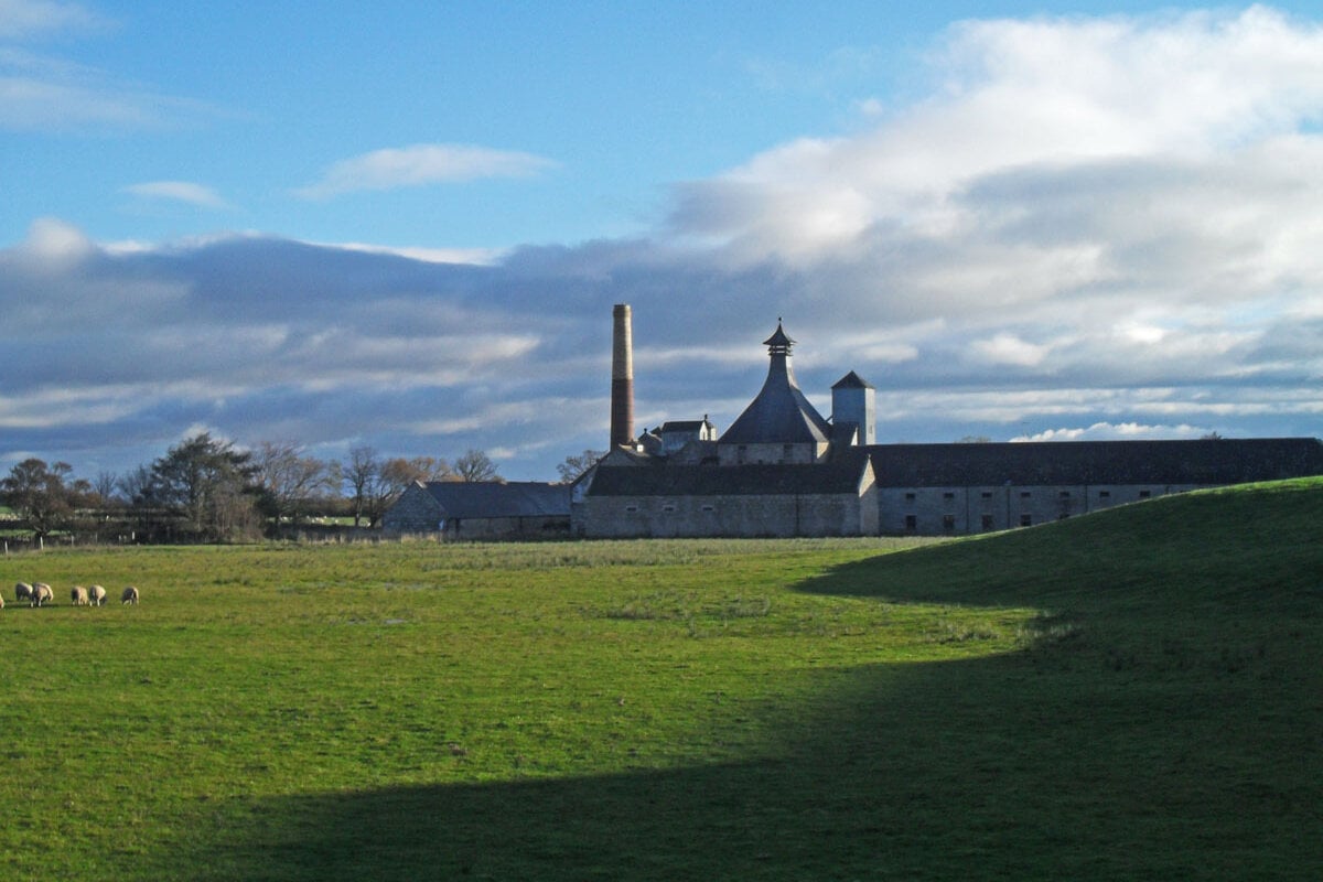Nhà chưng cất Brora với ống khói và mái chóp giữa đồng cỏ xanh ở Sutherland, Scotland