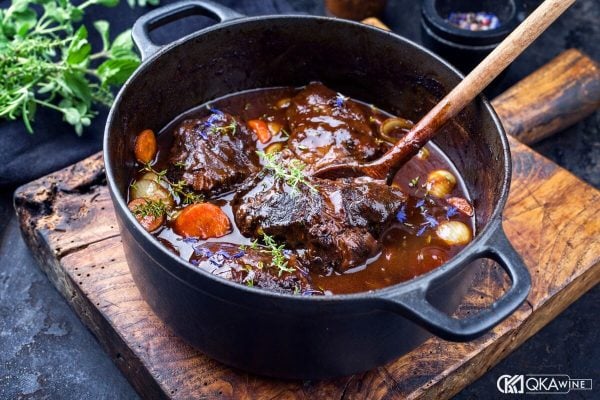 Nồi gang đựng bò hầm vang với cà rốt và hành trên thớt gỗ