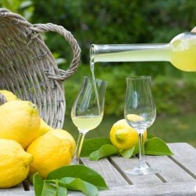 Rót limoncello từ chai vào ly nhỏ cạnh giỏ chanh vàng