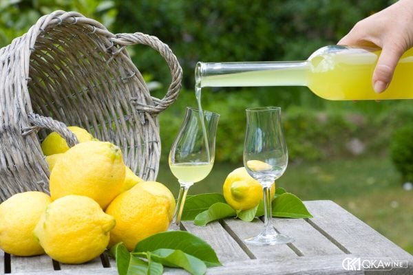 Rót limoncello từ chai vào ly nhỏ cạnh giỏ chanh vàng
