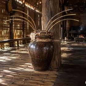 Ché rượu cần gốm nâu cắm nhiều cần trúc trong nhà sàn