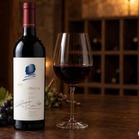 Chai Opus One nhãn kem, hai chân dung nghiêng xanh cạnh ly vang lớn