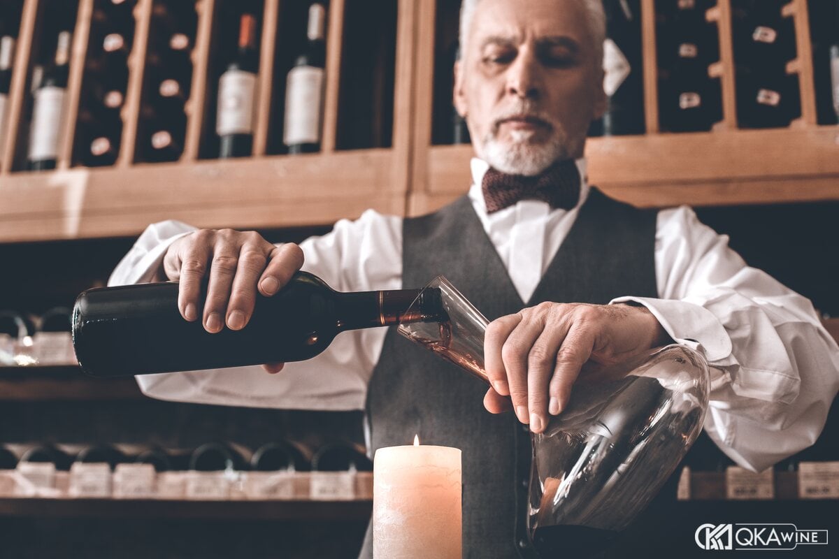 Sommelier chiết vang đỏ sang bình decanter trước ngọn nến