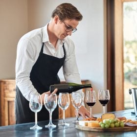 Sommelier đeo tạp dề rót vang vào dãy ly trên bàn
