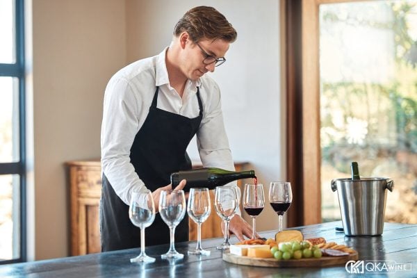 Sommelier đeo tạp dề rót vang vào dãy ly trên bàn